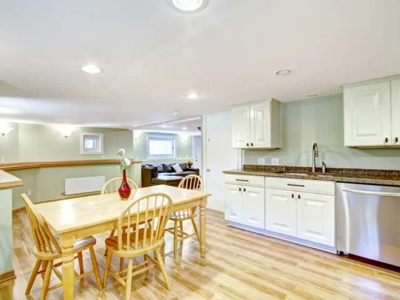 Basement kitchen room with rustic dining table set in Mother-in-law apartment. Light mint tones of wall blent with white kitchen cabinets